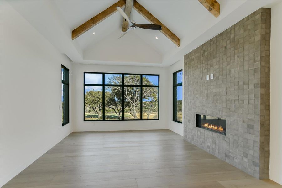 Unfurnished living room featuring a tile fireplace, light wood-type flooring, a ceiling fan, and healthy amount of natural light