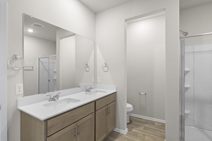 Image of a primary bathroom with a white jack and jill countertop, brown cabinets, a large mirror and a semi-private water closet Image of a primary bathroom with a white jack and jill countertop, brown cabinets, a large mirror and a semi-private water closet