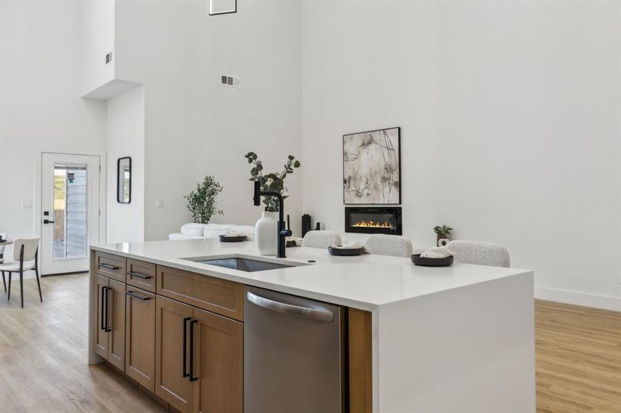 Kitchen featuring stainless steel dishwasher, sink, a high ceiling, a fireplace, and a kitchen island with sink