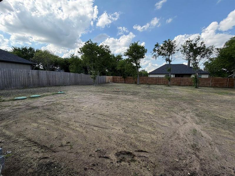 Spacious backyard area featuring a wood fence perimeter and several young trees