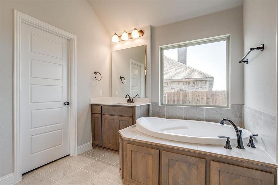 Bathroom with tile patterned floors, vaulted ceiling, vanity, and a bathtub