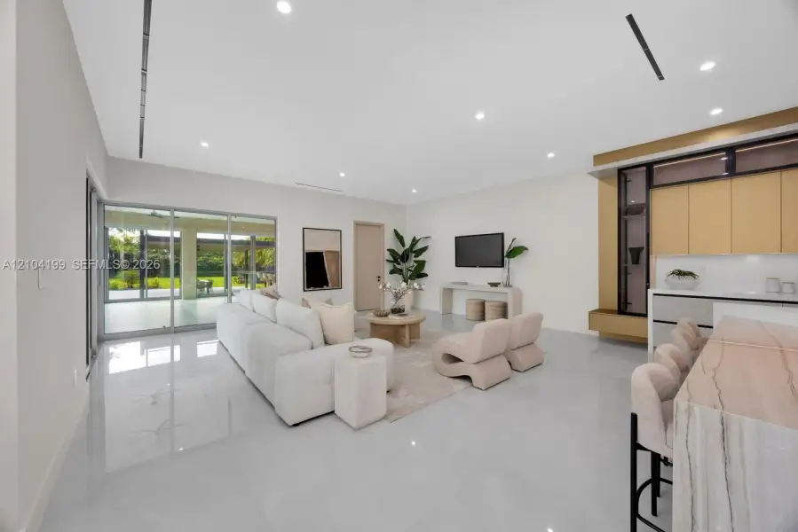 Open-concept living space featuring large-format tile flooring, recessed linear lighting, sliding glass walls, and custom cabinetry with stone-surfaced waterfall island