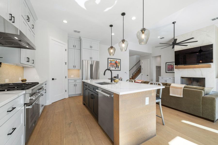Kitchen with a high end fireplace, a kitchen breakfast bar, white cabinets, appliances with stainless steel finishes, and decorative light fixtures