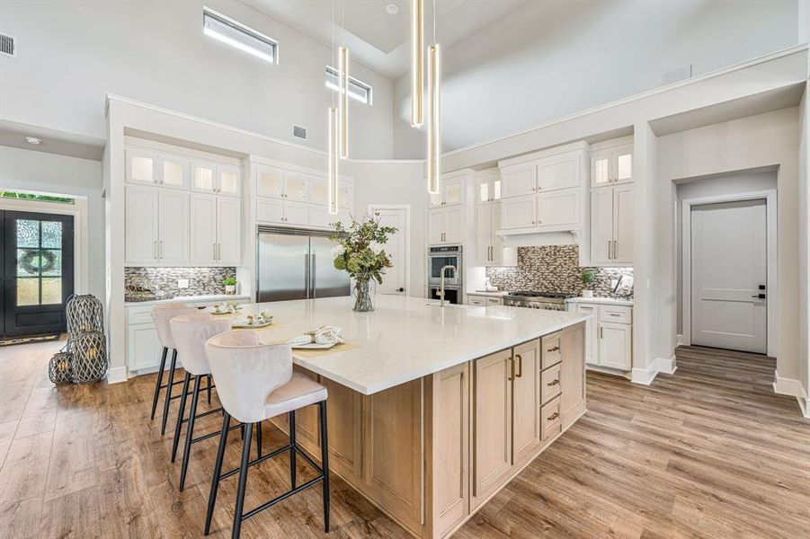 Kitchen with light hardwood / wood-style flooring, stainless steel appliances, pendant lighting, a high ceiling, and a large island