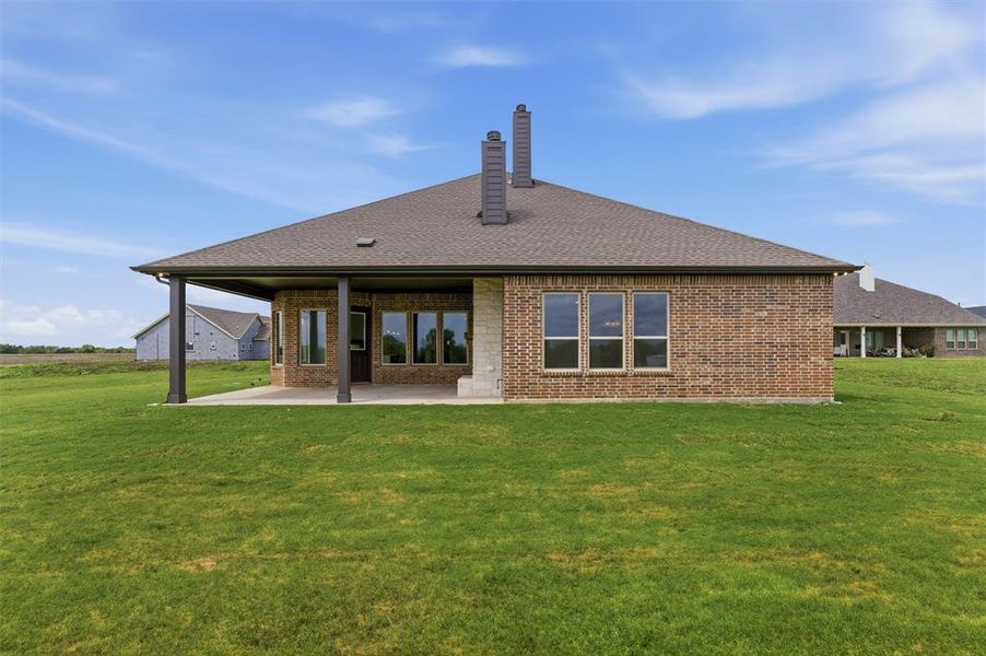 Back of property with a chimney, a patio area, a lawn, brick siding, and a shingled roof