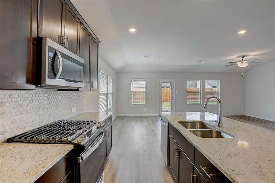 Kitchen with tasteful backsplash, stainless steel appliances, sink, light hardwood / wood-style floors, and ceiling fan