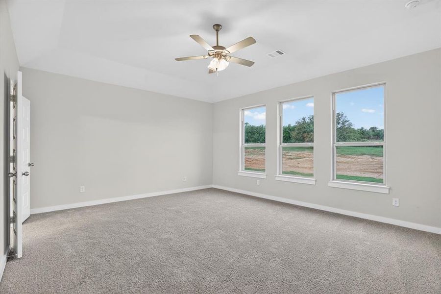Spacious room featuring three large windows, vaulted ceiling, neutral gray carpet, pale gray wall paint, and a ceiling fan with integrated lighting