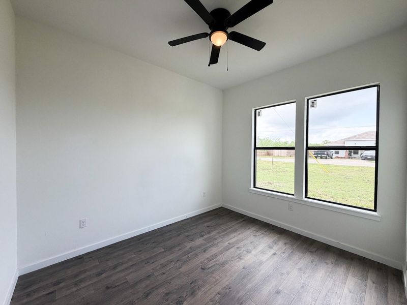 Interior space featuring wood-finish flooring, two large windows with black framing, and a ceiling fan with integrated lighting Interior space featuring wood-finish flooring, two large windows with black framing, and a ceiling fan with integrated lighting