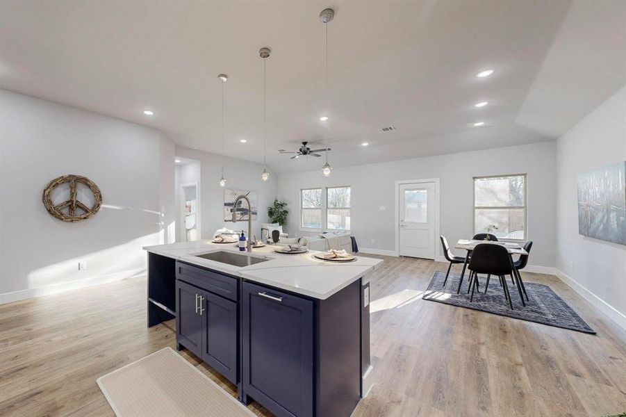 Kitchen featuring sink, decorative light fixtures, light hardwood / wood-style floors, and an island with sink