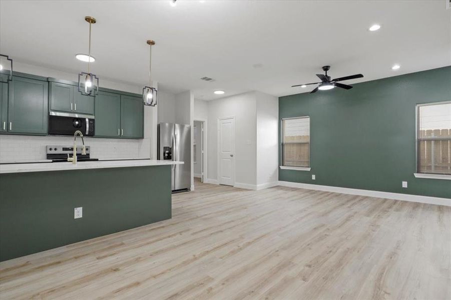 Kitchen with decorative backsplash, light wood-type flooring, stainless steel appliances, ceiling fan, and decorative light fixtures