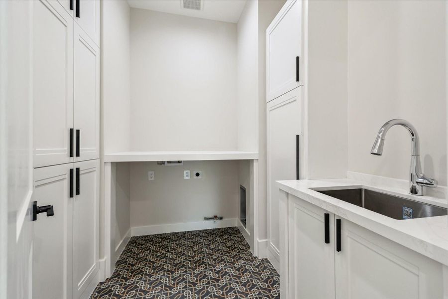 This Utility room showcases decorative tile floor, quartz countertops, a large stainless sink, and sleek cabinetry. Ample built-ins make it as functional as it is stylish.