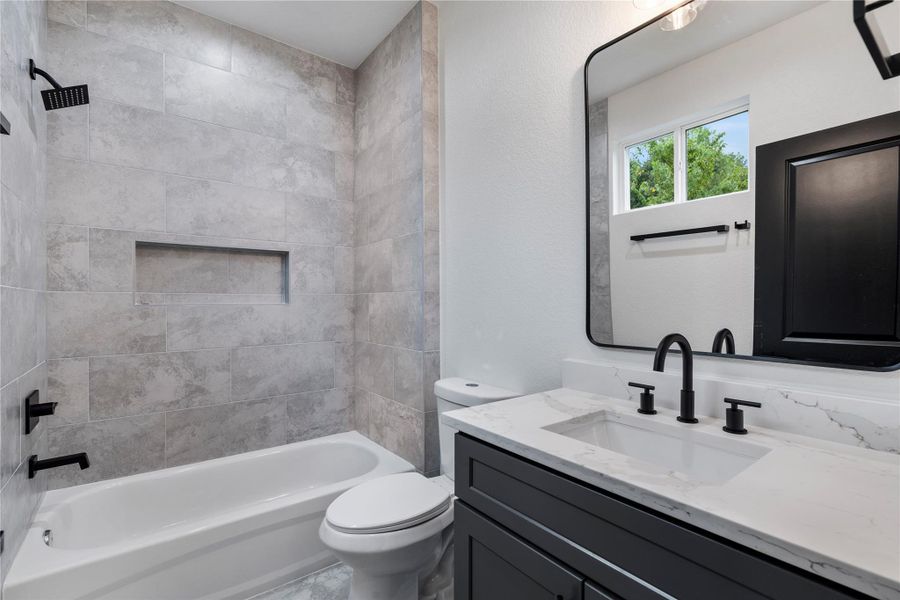 Secondary bath with quartz vanity, matte black fixtures, and a tiled shower-tub combo featuring a built-in niche. Secondary bath with quartz vanity, matte black fixtures, and a tiled shower-tub combo featuring a built-in niche.