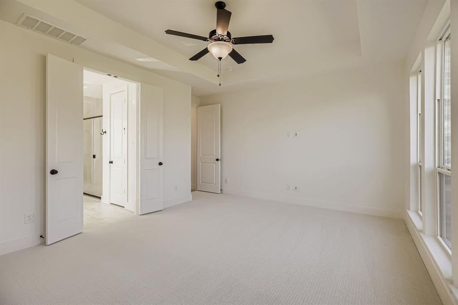Unfurnished bedroom with a raised ceiling, light colored carpet, and a ceiling fan Unfurnished bedroom with a raised ceiling, light colored carpet, and a ceiling fan