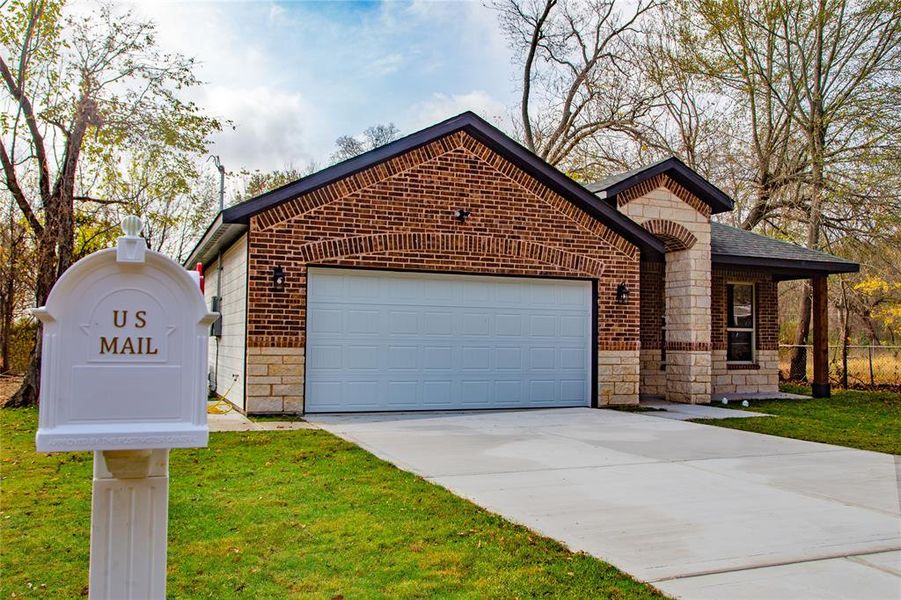 View of front facade with stone siding, driveway, brick siding, and a front lawn