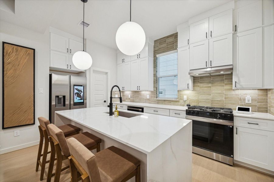 Large waterfall-edge island anchors the kitchen, offering generous workspace and seating. Matte black fixtures, quartz surfaces, and subtle tile accents lend a polished, modern aesthetic while maintaining a comfortable, inviting feel that connects seamlessly to the living area. Large waterfall-edge island anchors the kitchen, offering generous workspace and seating. Matte black fixtures, quartz surfaces, and subtle tile accents lend a polished, modern aesthetic while maintaining a comfortable, inviting feel that connects seamlessly to the living area.