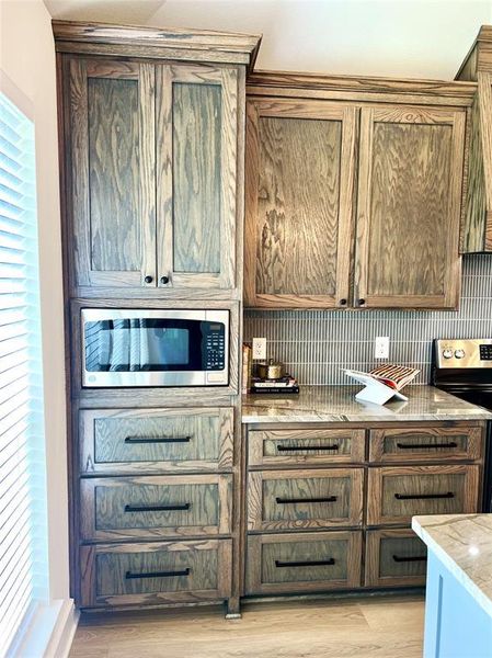 Kitchen featuring range with electric cooktop, backsplash, light stone counters, light wood-type flooring, and stainless steel microwave Kitchen featuring range with electric cooktop, backsplash, light stone counters, light wood-type flooring, and stainless steel microwave