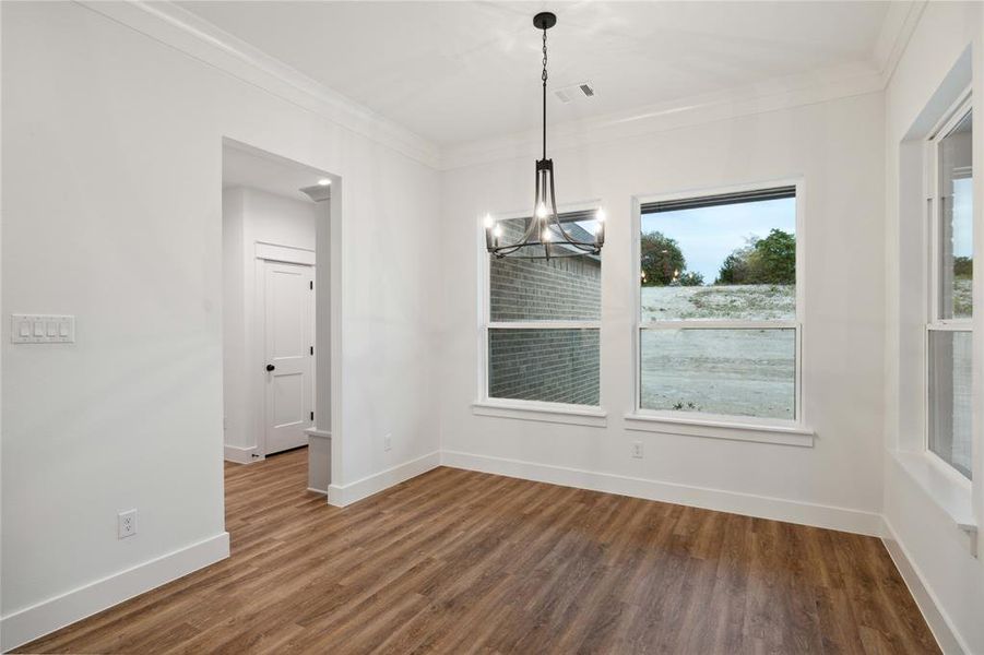 Unfurnished dining area with dark wood-type flooring, ornamental molding, and an inviting chandelier