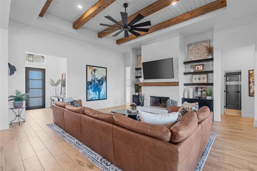 Living room with ceiling fan, a fireplace, beamed ceiling, and light hardwood / wood-style floors