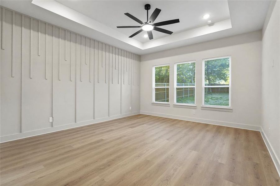 Empty room with a raised ceiling, light wood finished floors, a ceiling fan, and recessed lighting