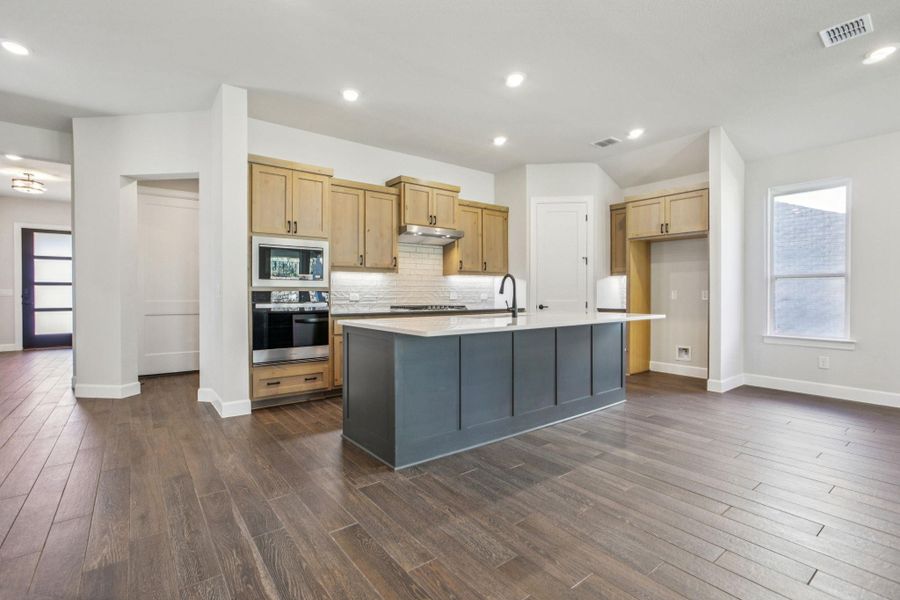 Kitchen featuring recessed lighting, stainless steel oven, decorative backsplash, an island with sink, and dark wood-type flooring Kitchen featuring recessed lighting, stainless steel oven, decorative backsplash, an island with sink, and dark wood-type flooring