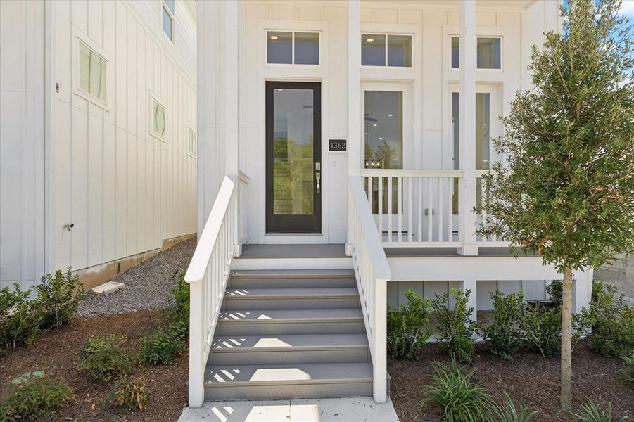 Inviting front entry featuring a dark-framed glass door, white board and batten siding, a covered porch with white railings, and a mature tree