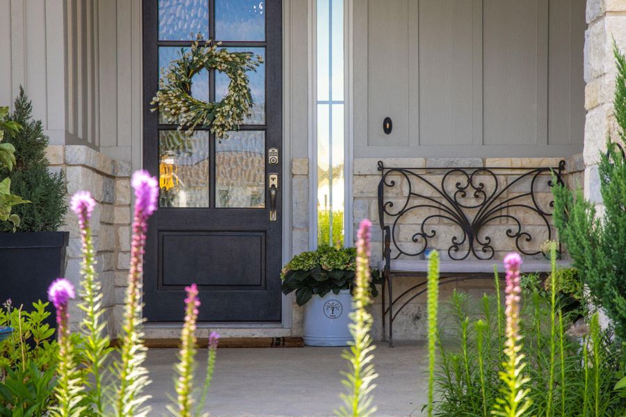 A welcoming front entry features a dark-paneled door, decorative wreath, and a charming wrought-iron bench.