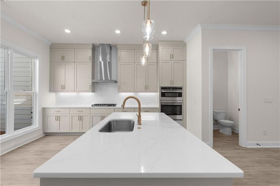 Kitchen featuring light wood-type flooring, tasteful backsplash, light stone counters, hanging light fixtures, and crown molding