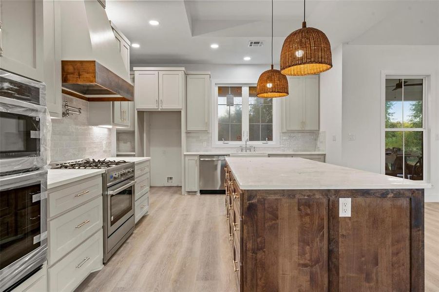 Kitchen with recessed lighting, stainless steel appliances, decorative light fixtures, light wood-type flooring, and custom range hood Kitchen with recessed lighting, stainless steel appliances, decorative light fixtures, light wood-type flooring, and custom range hood