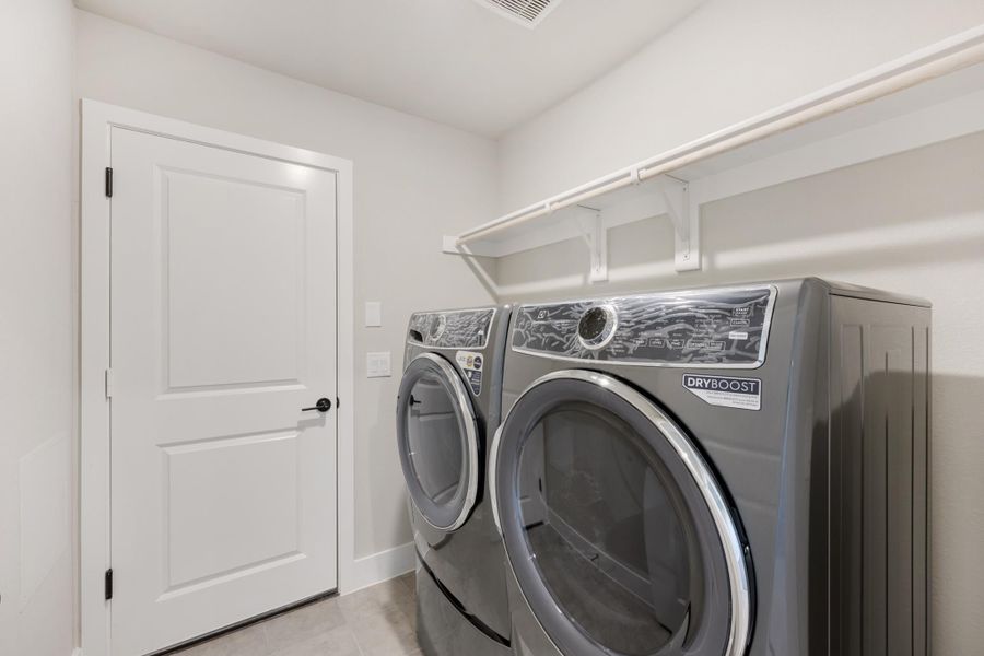 Laundry room with gray front-load washer and dryer set, white walls, and overhead shelf.