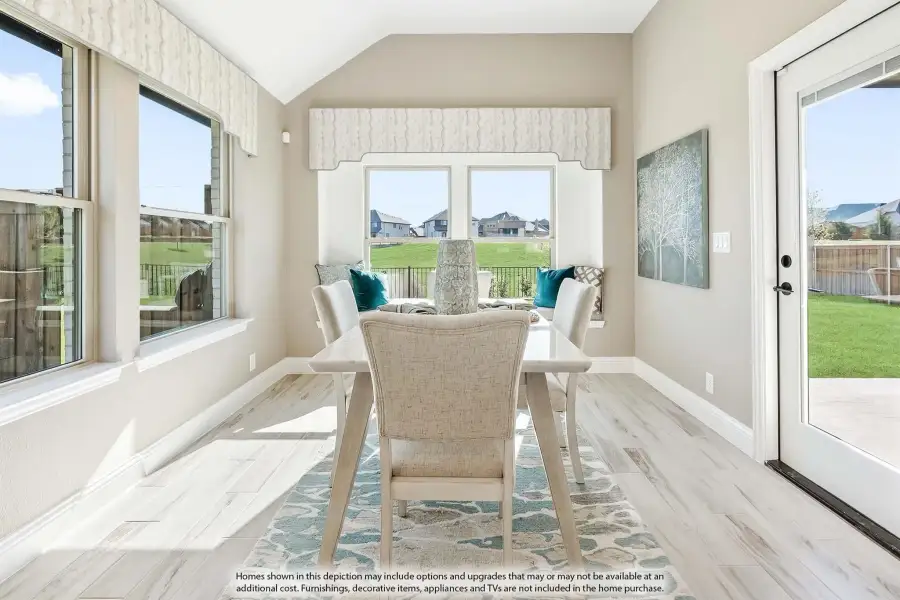 Bright dining area with vaulted ceiling, large windows, light wood floors, and patio door overlooking backyard