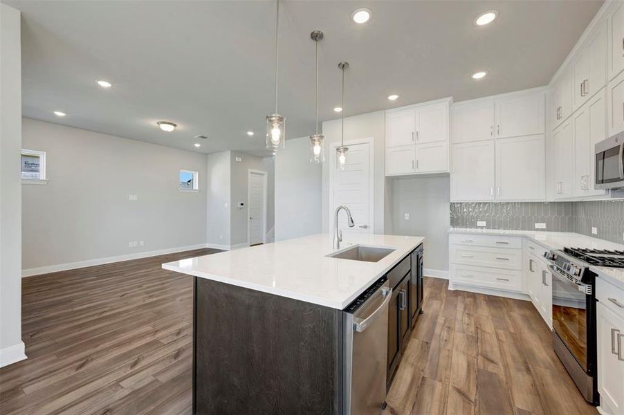 Dual tone kitchen featuring stainless steel appliances, dual tone cabinets, light stone counters, a kitchen island with sink, and light wood-type flooring