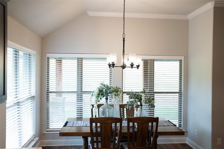 Dining room featuring a notable chandelier, dark hardwood / wood-style flooring, lofted ceiling, and crown molding