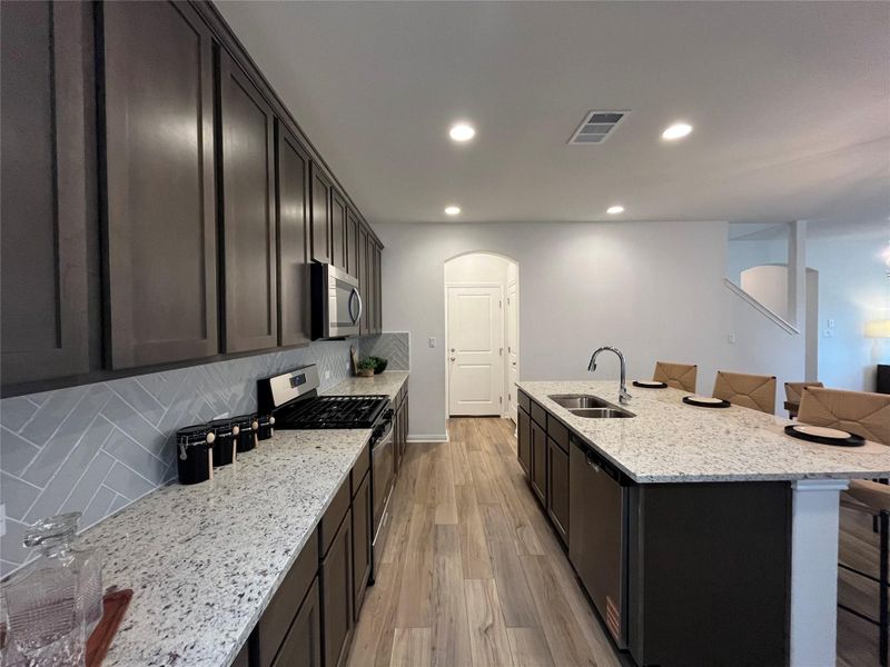 Kitchen featuring a breakfast bar area, appliances with stainless steel finishes, light stone countertops, decorative backsplash, and recessed lighting