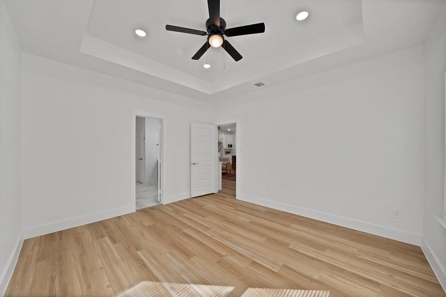 Unfurnished bedroom featuring a raised ceiling, recessed lighting, light wood finished floors, a ceiling fan, and ensuite bathroom