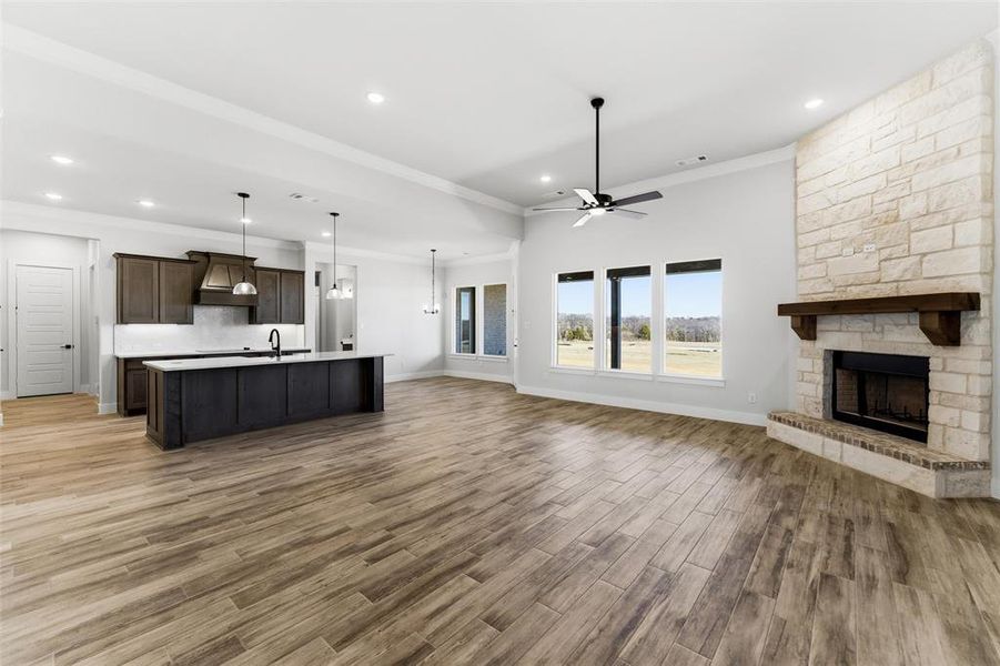 Unfurnished living room with crown molding, dark wood finished floors, a ceiling fan, a stone fireplace, and recessed lighting