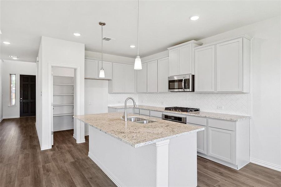 Kitchen featuring dark wood-type flooring, a center island with sink, stainless steel appliances, sink, and tasteful backsplash