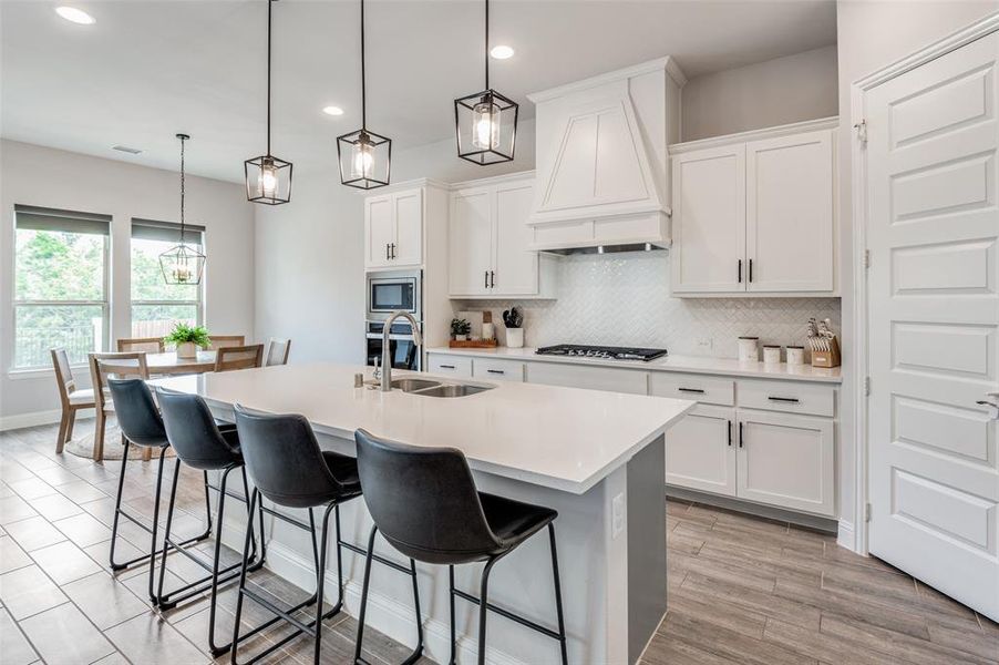 Kitchen featuring appliances with stainless steel finishes, decorative light fixtures, custom exhaust hood, and sink