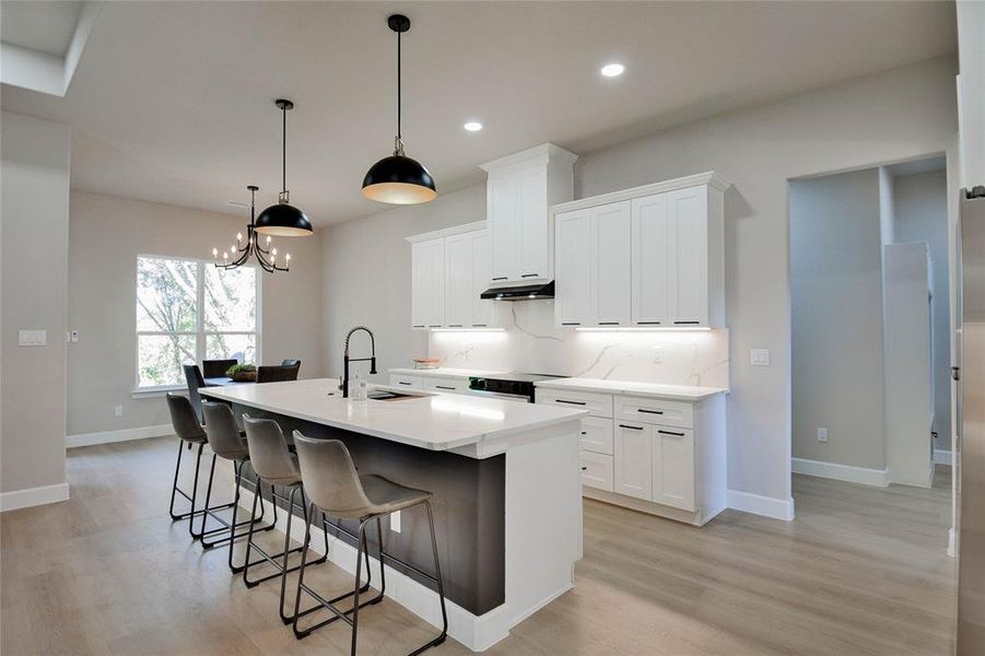 Kitchen with a center island with sink, a kitchen breakfast bar, white cabinetry, hanging light fixtures, and a chandelier Kitchen with a center island with sink, a kitchen breakfast bar, white cabinetry, hanging light fixtures, and a chandelier