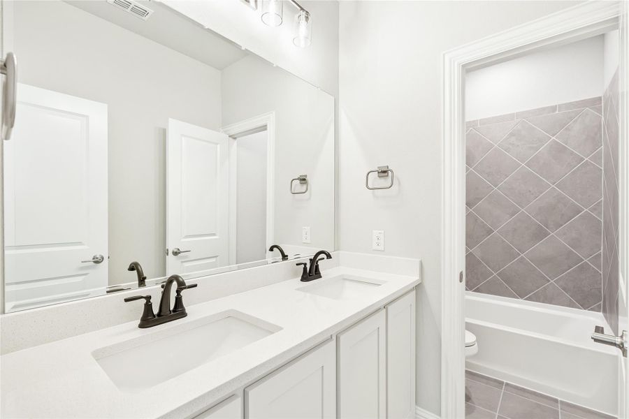 Bathroom with double sink vanity, white countertops, and tub-shower combo with gray tile surround Bathroom with double sink vanity, white countertops, and tub-shower combo with gray tile surround
