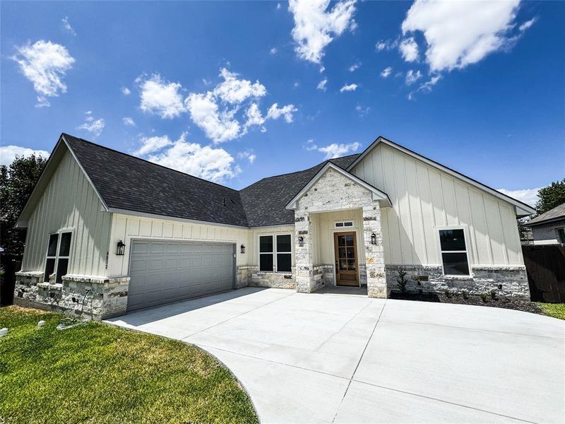 Modern inspired farmhouse featuring board and batten siding, a garage, stone siding, and concrete driveway Modern inspired farmhouse featuring board and batten siding, a garage, stone siding, and concrete driveway