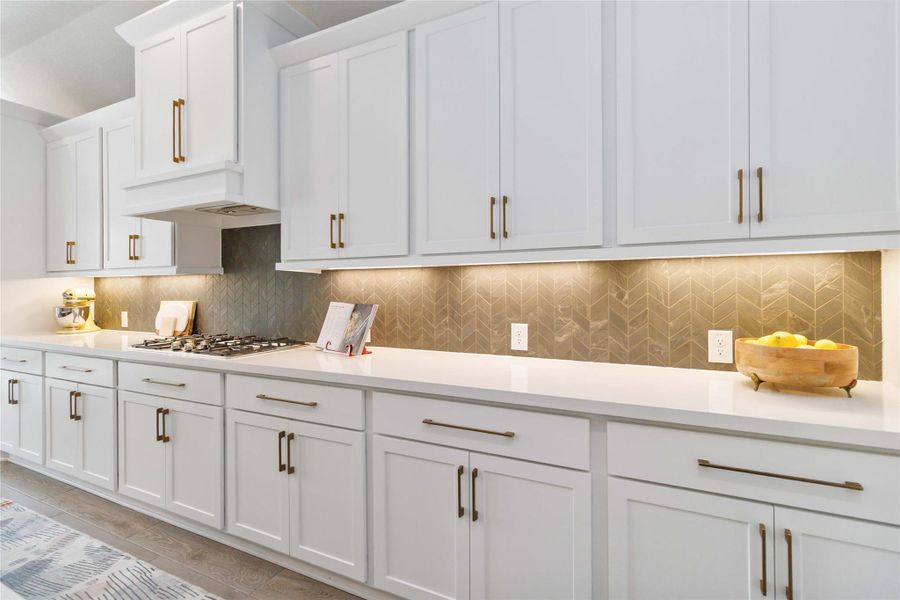 Kitchen with backsplash, white cabinetry, light stone countertops, and stainless steel gas cooktop Kitchen with backsplash, white cabinetry, light stone countertops, and stainless steel gas cooktop