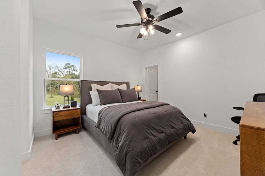 Another secondary bedroom that features a dark stained ceiling fan, natural light and walk in closet.