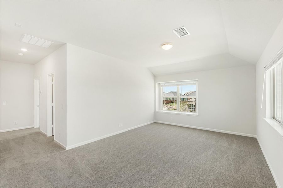 Empty bedroom with vaulted ceiling, gray carpet, and a window overlooking the neighborhood