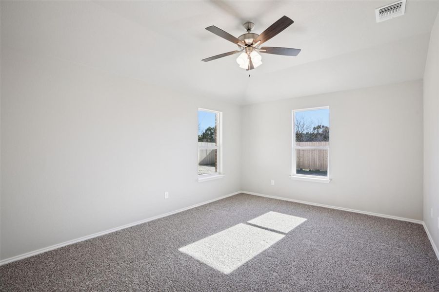 Carpeted empty room featuring plenty of natural light, lofted ceiling, and a ceiling fan