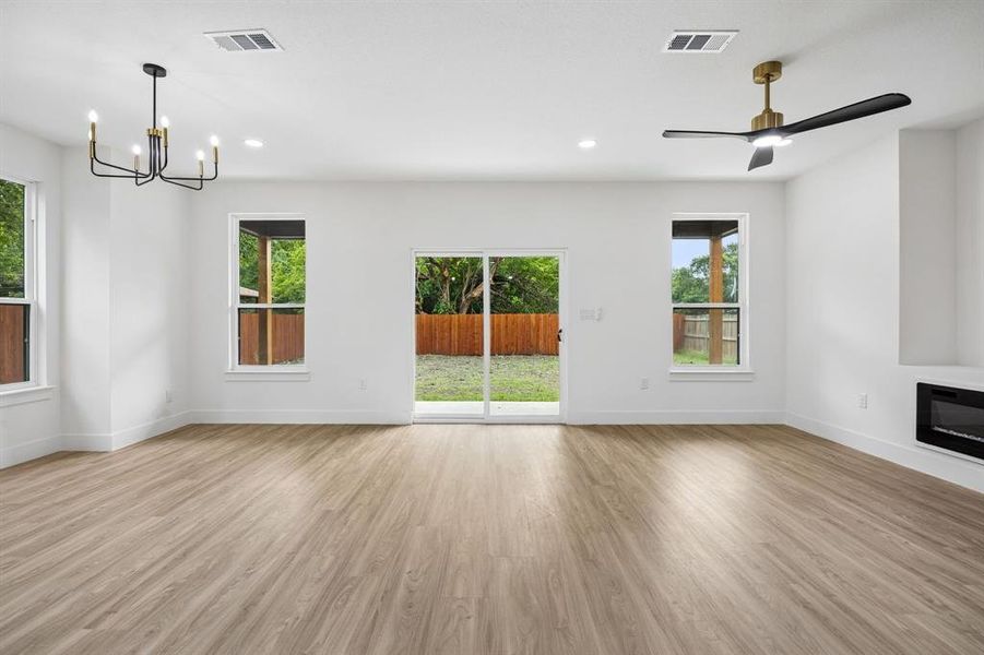 Spacious room featuring wood-finish flooring, recessed lighting, and a modern chandelier Spacious room featuring wood-finish flooring, recessed lighting, and a modern chandelier