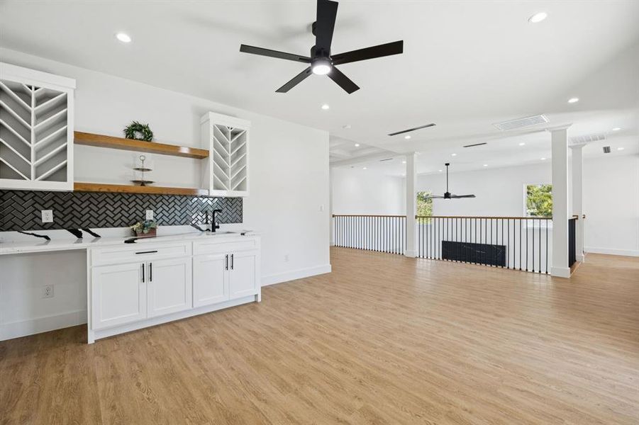 Bar area featuring a ceiling fan, white cabinets, decorative backsplash, open shelves, and light wood finished floors