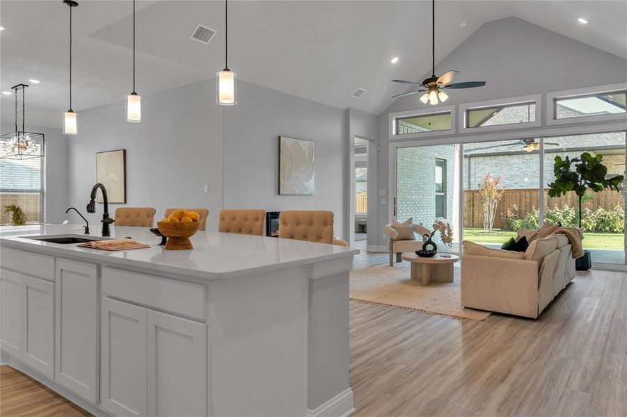 Kitchen featuring hanging light fixtures, light wood-style flooring, open floor plan, high vaulted ceiling, and white cabinets Kitchen featuring hanging light fixtures, light wood-style flooring, open floor plan, high vaulted ceiling, and white cabinets