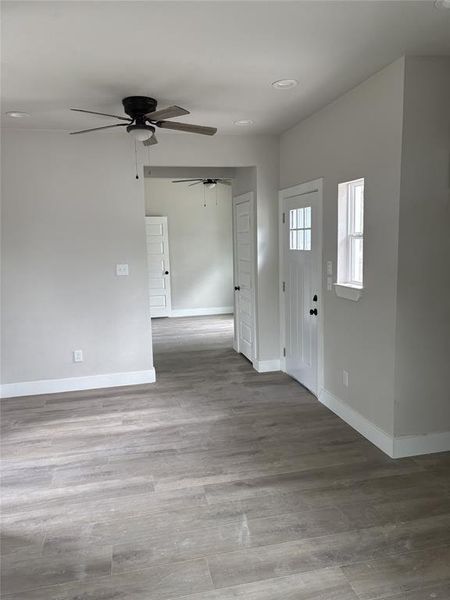 Light-filled interior featuring wood-finish flooring, recessed lighting, ceiling fan, white baseboards, and a paneled front door with divided lites Light-filled interior featuring wood-finish flooring, recessed lighting, ceiling fan, white baseboards, and a paneled front door with divided lites