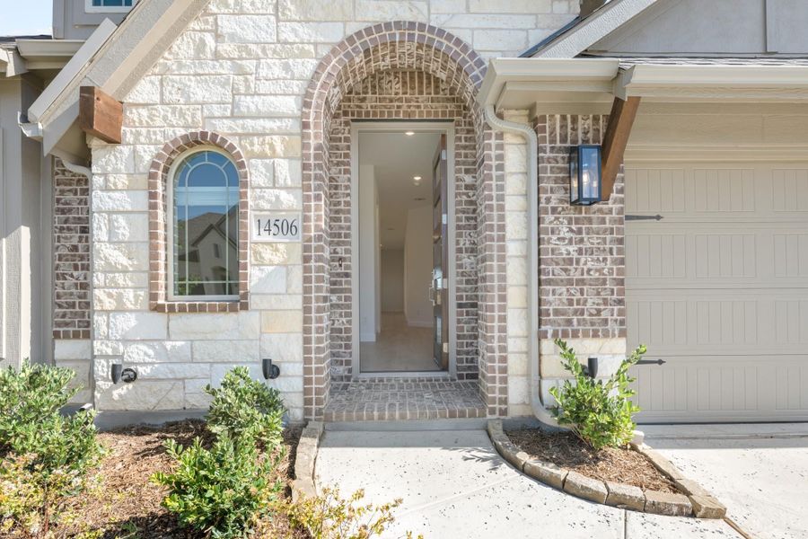 Home entrance with brick arched doorway, stone facade, arched window, and attached garage at 14506