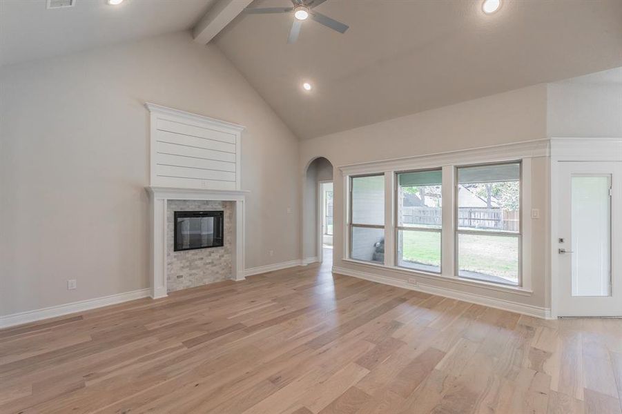 Unfurnished living room featuring beamed ceiling, ceiling fan, light hardwood / wood-style floors, and a fireplace